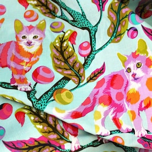 May include: A light blue fabric featuring a repeating pattern of kittens with pink, orange, and white fur. The kittens are positioned among stylized teal branches, large green and brown leaves, and small round pink and orange fruit-like shapes.