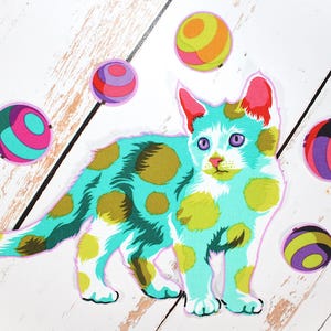 May include: A colorful cat-shaped sticker with a turquoise body and yellow-brown spots. The cat has pink ears and purple eyes. Several round, striped stickers in various colors surround the cat, creating a playful, whimsical design.