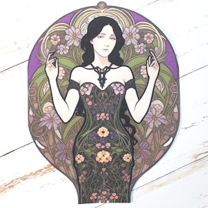 May include: A woman in a black dress with floral embroidery stands in a decorative frame. The frame is filled with stylised flowers and leaves in shades of green, purple, and brown.
