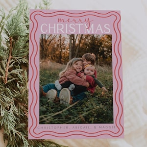 Könnte beinhalten: Eine rosa Weihnachtskarte mit einem wellenförmigen Rand und den Worten "merry CHRISTMAS" in einer Schreibschrift. Die Karte zeigt ein Foto von drei Kindern auf einem Feld. Die Namen "CHRISTOPHER, ABIGAIL, & MAGGIE" sind unten aufgedruckt.