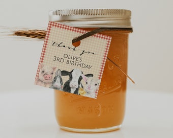 May include: A small glass jar filled with a yellow liquid, tied with a brown ribbon and a thank you tag that says "Thank you Olive's 3rd Birthday". The tag has a red and white checkered background and features a cartoon illustration of farm animals.