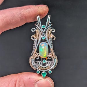 May include: A silver and gold wire wrapped pendant featuring a large oval opal gemstone surrounded by smaller green gemstones.