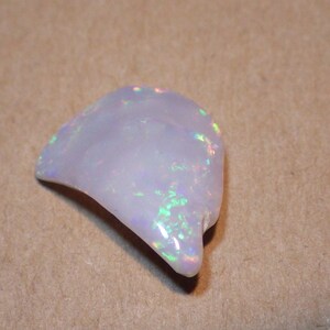 May include: A white opal gemstone with iridescent rainbow flashes. The opal is a rough, natural stone with an irregular shape.