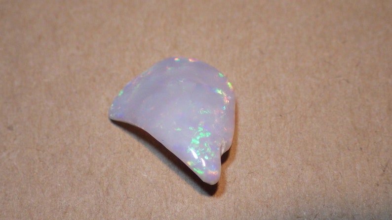 May include: A white opal gemstone with iridescent rainbow flashes. The opal is a rough, natural stone with an irregular shape.