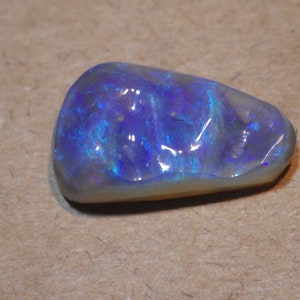 May include: A blue and gray opal gemstone with a rough, irregular shape.