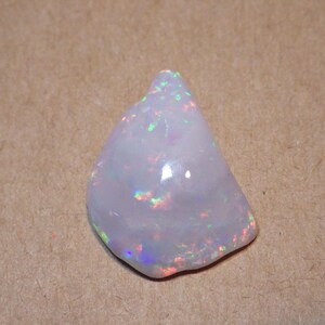 May include: A white opal gemstone with iridescent rainbow flashes. The opal is a rough, natural stone with an irregular shape.