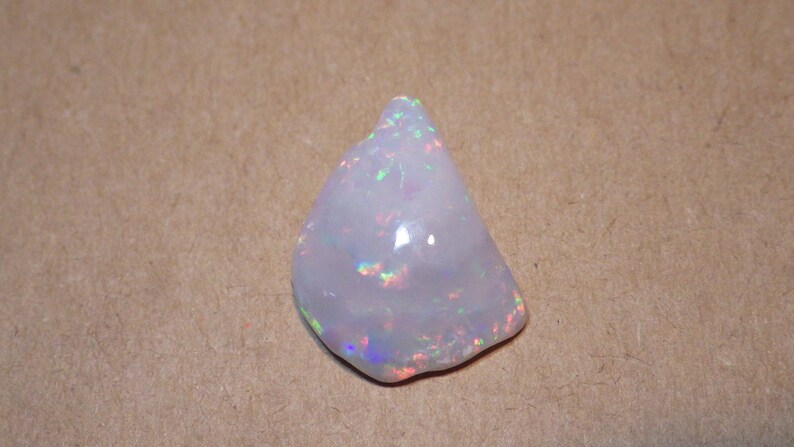 May include: A white opal gemstone with iridescent rainbow flashes. The opal is a rough, natural stone with an irregular shape.