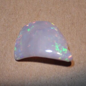 May include: A white opal gemstone with iridescent flashes of color. The opal is irregularly shaped and has a smooth, polished surface.