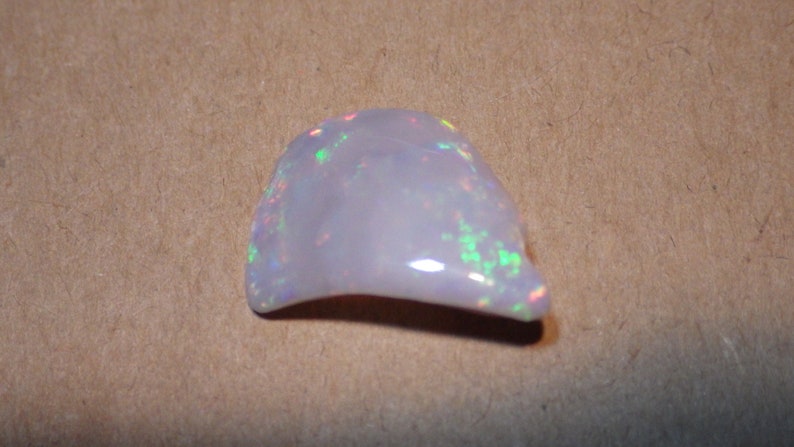 May include: A white opal gemstone with iridescent flashes of color. The opal is irregularly shaped and has a smooth, polished surface.