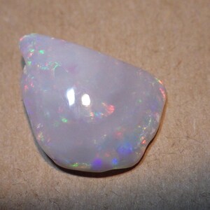 May include: A white opal gemstone with iridescent flashes of color. The opal is irregularly shaped and has a smooth, polished surface.