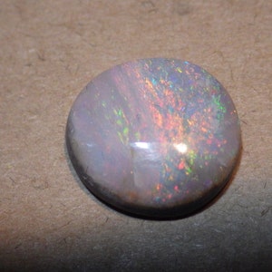 May include: A round, white opal gemstone with iridescent flashes of color, including pink, green, and blue.