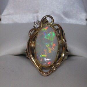 May include: A gold ring with an oval opal gemstone and a small diamond accent. The ring has a delicate, ornate design.