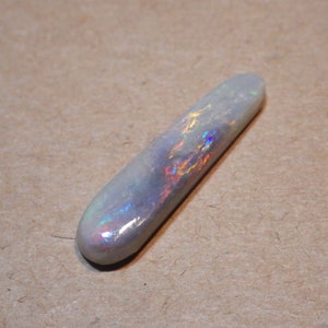 May include: A long, white opal cabochon with iridescent rainbow flashes. The opal is smooth and polished.