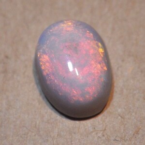 May include: Oval-shaped opal gemstone with a pearly white base and internal flashes of orange and yellow. The polished stone has a smooth, reflective surface, showcasing its natural beauty. A close-up view highlights the play of color.