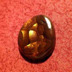 May include: A brown and gold agate gemstone with a unique, intricate pattern. The gemstone is smooth and polished, with a glossy finish.