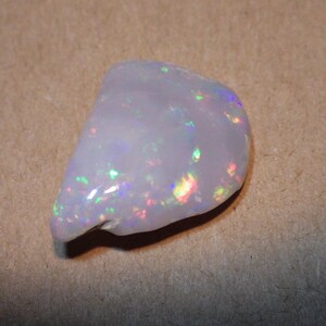 May include: A white opal gemstone with iridescent rainbow flashes. The opal is a rough, natural stone with an irregular shape.