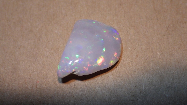 May include: A white opal gemstone with iridescent rainbow flashes. The opal is a rough, natural stone with an irregular shape.