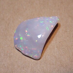 May include: A white opal gemstone with iridescent flashes of color. The opal is a natural stone with a smooth, polished surface.