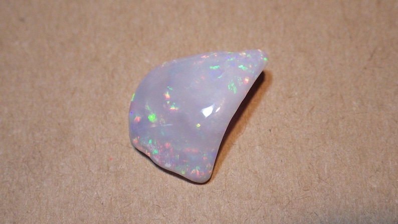 May include: A white opal gemstone with iridescent flashes of color. The opal is a natural stone with a smooth, polished surface.