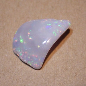May include: A white opal gemstone with iridescent flashes of color. The opal is a natural stone with a smooth, polished surface.