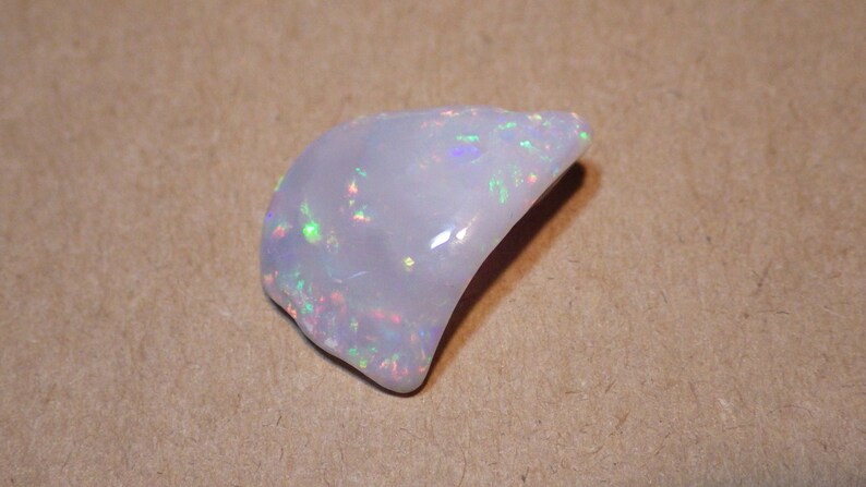 May include: A white opal gemstone with iridescent flashes of color. The opal is a natural stone with a smooth, polished surface.
