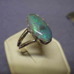 May include: A silver ring with a large oval-shaped opal gemstone. The opal has a green and blue iridescent sheen.