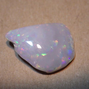 May include: A white opal gemstone with iridescent flashes of color. The opal is a rough, natural stone with an irregular shape.