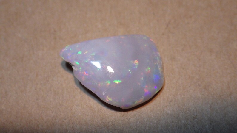 May include: A white opal gemstone with iridescent flashes of color. The opal is a rough, natural stone with an irregular shape.