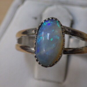 May include: A silver ring with a white opal gemstone set in a silver bezel. The opal has a blue and green iridescent sheen.