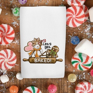 May include: White kitchen towel with a red and white snowman and gingerbread man illustration. The text "Let's get baked!" is printed on the towel.