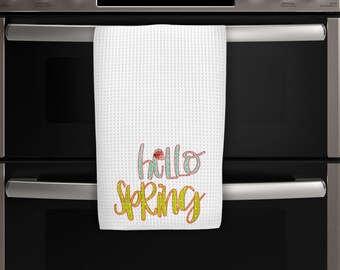 May include: White waffle weave kitchen towel with the text "hello spring" in colorful lettering. The towel is hanging on a stainless steel oven.