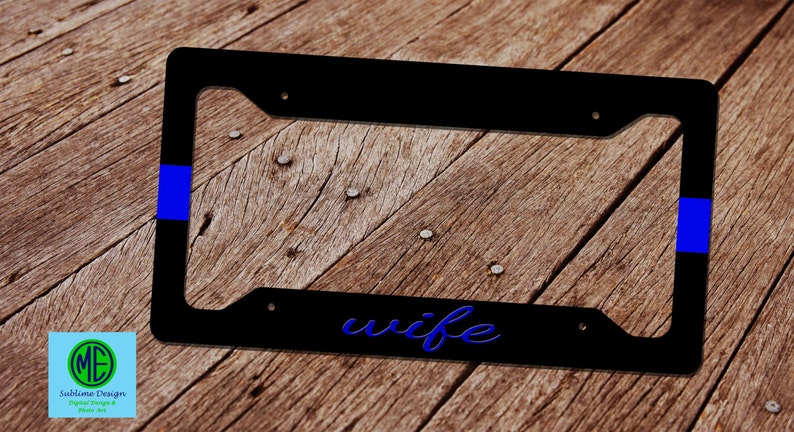 May include: Black license plate frame with the word "wife" in blue script. The frame has a blue stripe on the left and right sides. The background is a wooden surface.