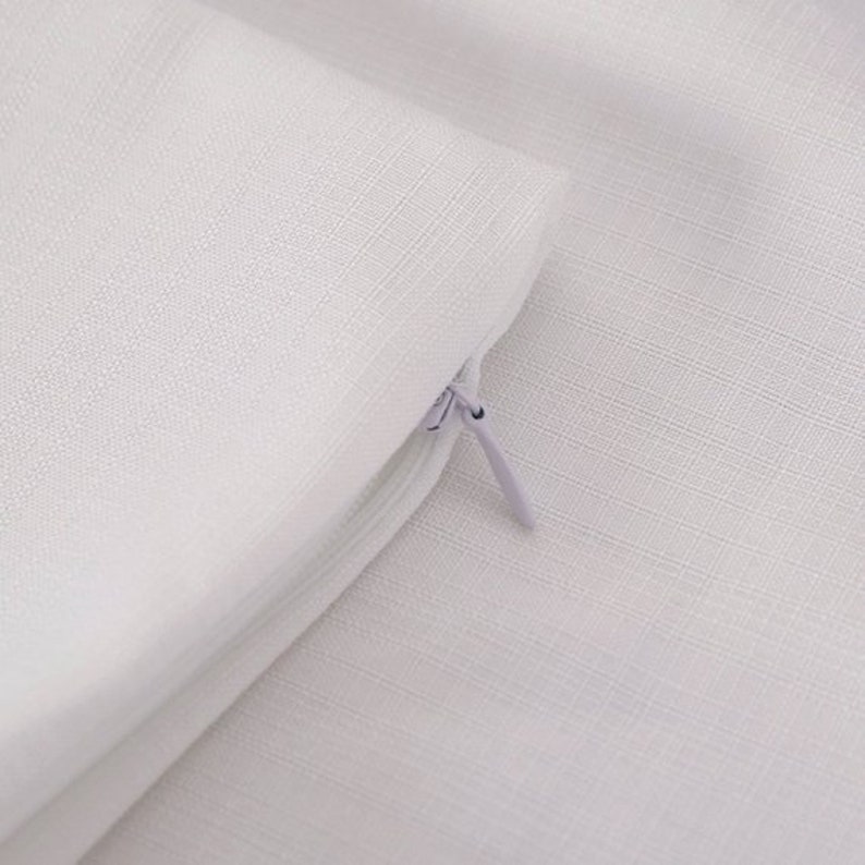 May include: Close-up of a white zipper on a white pillowcase. The zipper is partially open, revealing the white fabric inside.