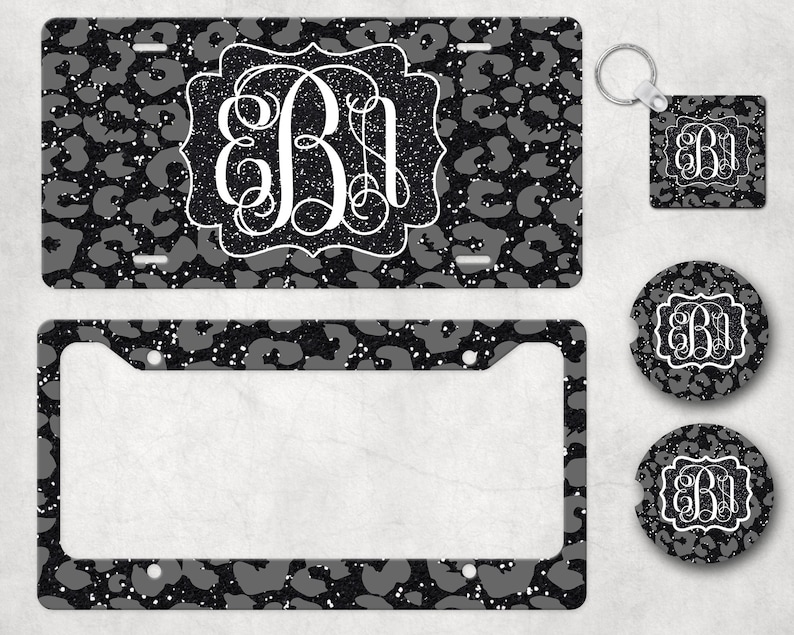 May include: A set of black and white leopard print car accessories featuring a monogrammed initial. The set includes a license plate frame, a keychain, a coaster, and a square sticker.