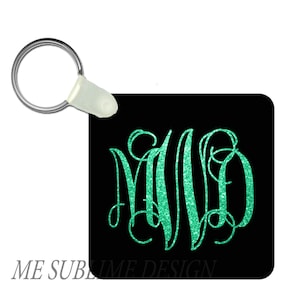 Puede incluir: Un llavero cuadrado negro con un anillo de llave plateado y un monograma "MVD" de purpurina verde.