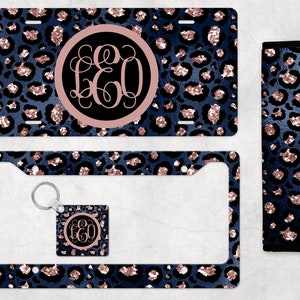 May include: A set of car accessories featuring a blue and rose gold leopard print design. The set includes a license plate frame, a license plate, a key chain, and a seatbelt strap.