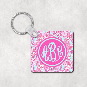 May include: A pink and blue floral patterned keychain with a silver key ring and a pink circle with a white monogram "ABC" in the center.
