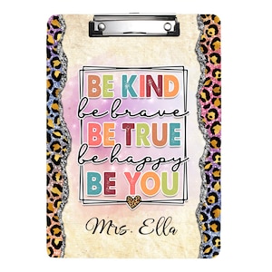Puede incluir: Un portapapeles con un diseño colorido que presenta el texto "Be Kind, Be Brave, Be True, Be Happy, Be You" y el nombre "Mrs. Ella". El fondo es un degradado rosa y blanco con un borde de estampado de leopardo.