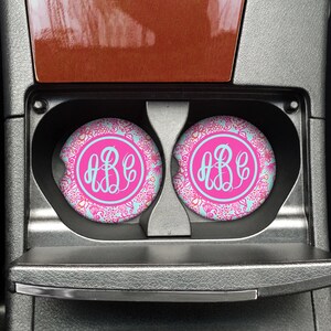 May include: Two pink and blue floral car coasters with a white monogram "ABC" in the center of each coaster.