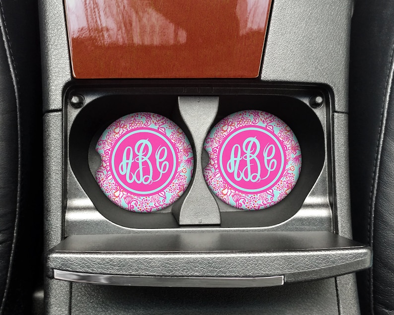 May include: Two pink and blue floral car coasters with a white monogram "ABC" in the center of each coaster.