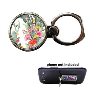 May include: A silver phone ring holder with a round, white background featuring a watercolor design of pink, red, and yellow flowers and green cactus plants. The text "phone not included" is printed below the ring holder.