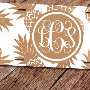 May include: A white personalized license plate with a gold pineapple design and the monogram "LLS" in a circle.