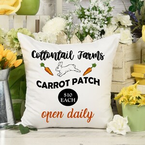 May include: White pillow with a black and white illustration of a rabbit running with carrots. The text on the pillow reads "Cottontail Farms Carrot Patch $10 Each open daily".