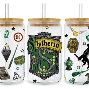May include: Three clear glass tumblers with bamboo lids and straws. Each tumbler features a different design with Harry Potter-themed graphics, including a Slytherin crest, a scarf, and a golden snitch. The tumblers are decorated with stars.