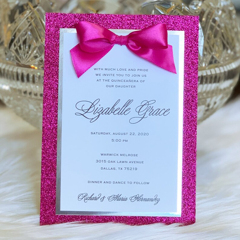 May include: Pink glitter card with a silver border and a white insert. The card has a pink bow on top and text that reads "WITH MUCH LOVE AND PRIDE WE INVITE YOU TO JOIN US AT THE QUINCEA&Ntilde;ERA OF OUR DAUGHTER Lizabelle Grace SATURDAY, AUGUST 22, 2020 5:00 PM WARWICK MELROSE 3015 OAK LAWN AVENUE DALLAS, TX 75219 DINNER AND DANCE TO FOLLOW Richard & Maria Hernandez"