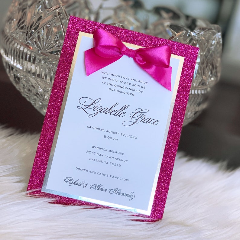 May include: Pink glitter card with a white border and a pink bow. The card has the text "WITH MUCH LOVE AND PRIDE WE INVITE YOU TO JOIN US AT THE QUINCEA&Ntilde;ERA OF OUR DAUGHTER Bizabelle Grace SATURDAY, AUGUST 22, 2020 5:00 PM WARWICK MELROSE 3015 OAK LAWN AVENUE DALLAS, TX 75219 DINNER AND DANCE TO FOLLOW Richard & Maria Hernandez".
