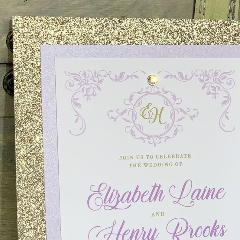 May include: A wedding invitation with a gold glitter background, a lavender border, and a white card with a purple floral design. The card says "Join us to celebrate the wedding of Elizabeth Laine and Henry Brooks".