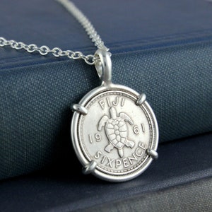 May include: Silver necklace with a silver coin pendant featuring a turtle and the text "FIJI 1961 SIXPENCE".