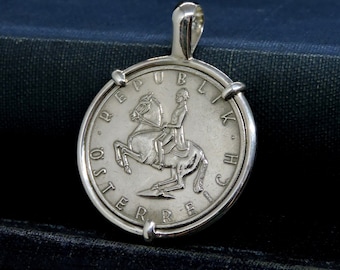 May include: Silver pendant featuring a replica of an Austrian coin with the inscription "REPUBLIK OSTERREICH" and a depiction of a rider on horseback.