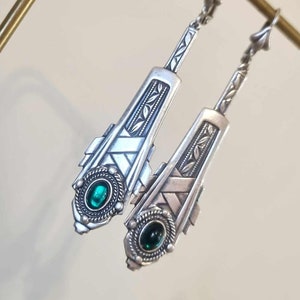 May include: A pair of silver dangle earrings with green gemstone accents. The earrings feature an intricate geometric design with a woven pattern.